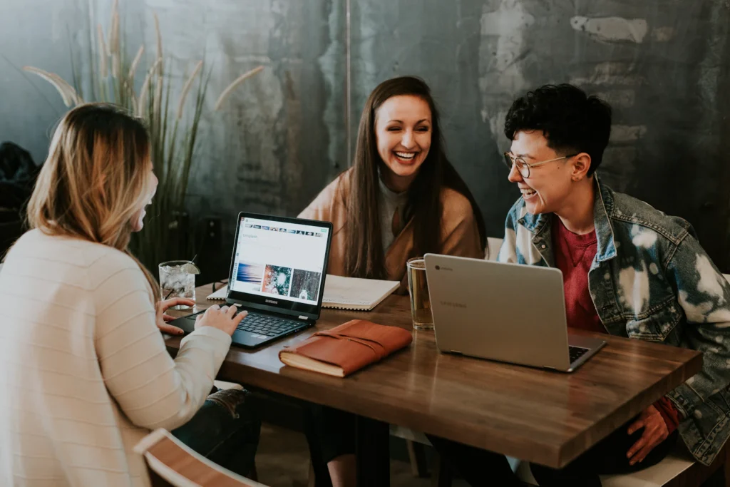 Three colleagues talking and laughing around a table with laptops