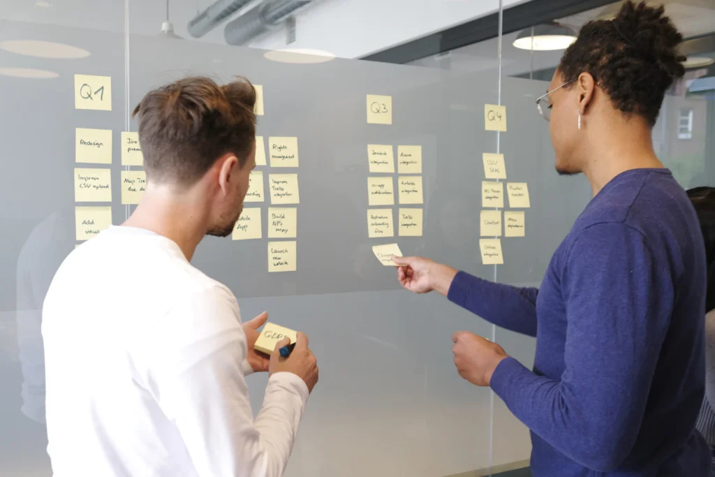 Two people planning a project with sticky notes on a glass wall